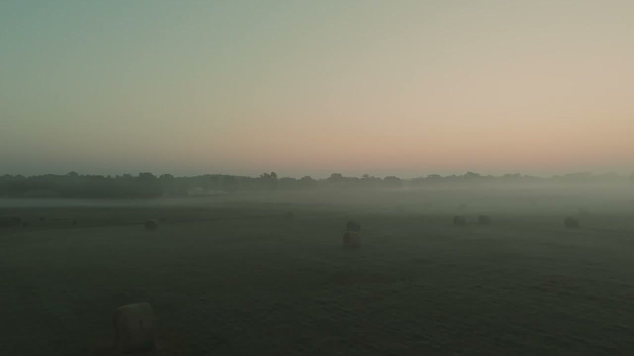 Misty dawn over the Ozark ranch — hay bales dot a sprawling pasture beneath a golden sunrise